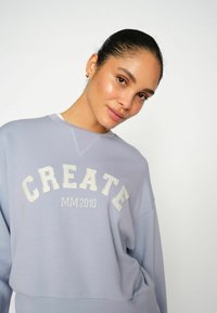 Sudadera de lavanda clara hecha de una tela suave, que presenta "CREATE" y "MM 2010" en letras blancas en la parte delantera. Diseño de cuello redondo.