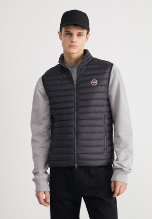 Gilet imbottito nero con pannelli laterali grigi, dotato di zip frontale, colletto alto e una patch con logo. Indossato sopra un maglione grigio.