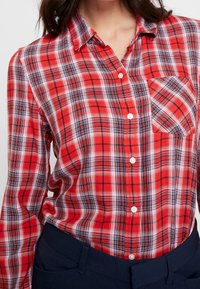 Chemise à carreaux rouges et noirs avec boutons, une seule poche poitrine, fabriquée en tissu léger, avec col et manches longues.