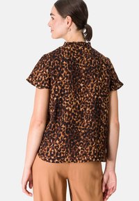 Bruine luipaardprint top met korte mouwen en een ronde halslijn, met een ontspannen pasvorm en een gladde textuur. Gemaakt in combinatie met beige broek.