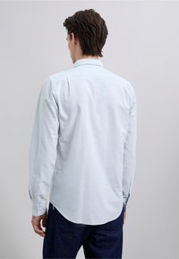 Lichtblauw overhemd met knopen, een gestructureerd patroon, lange mouwen en een kraag aan de achterkant. Afgeronde zoomlijn en manchetten met knopen.