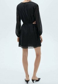 Czarna przezroczysta sukienka z długimi rękawami, w zygzakowy wzór, z talią ściągniętą i wycięciami po bokach. Gładka tekstura i długość ponad kolano.