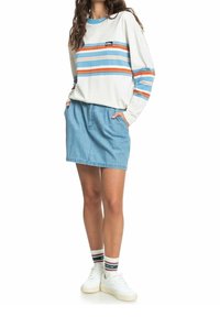 Vit långärmad skjorta med blå och orange ränder, kombinerad med en ljus denimkjol. Vita sneakers och flerfärgade strumpor fulländar looken.