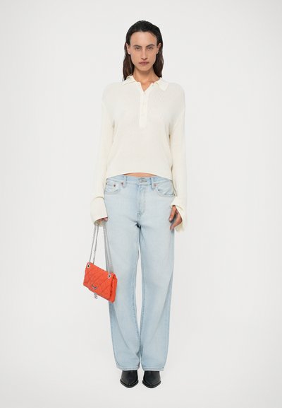 Cremefarvet ribstrikket sweater med krave, lyseblå lige jeans, sorte spidse sko og en lille orange quiltet taske.