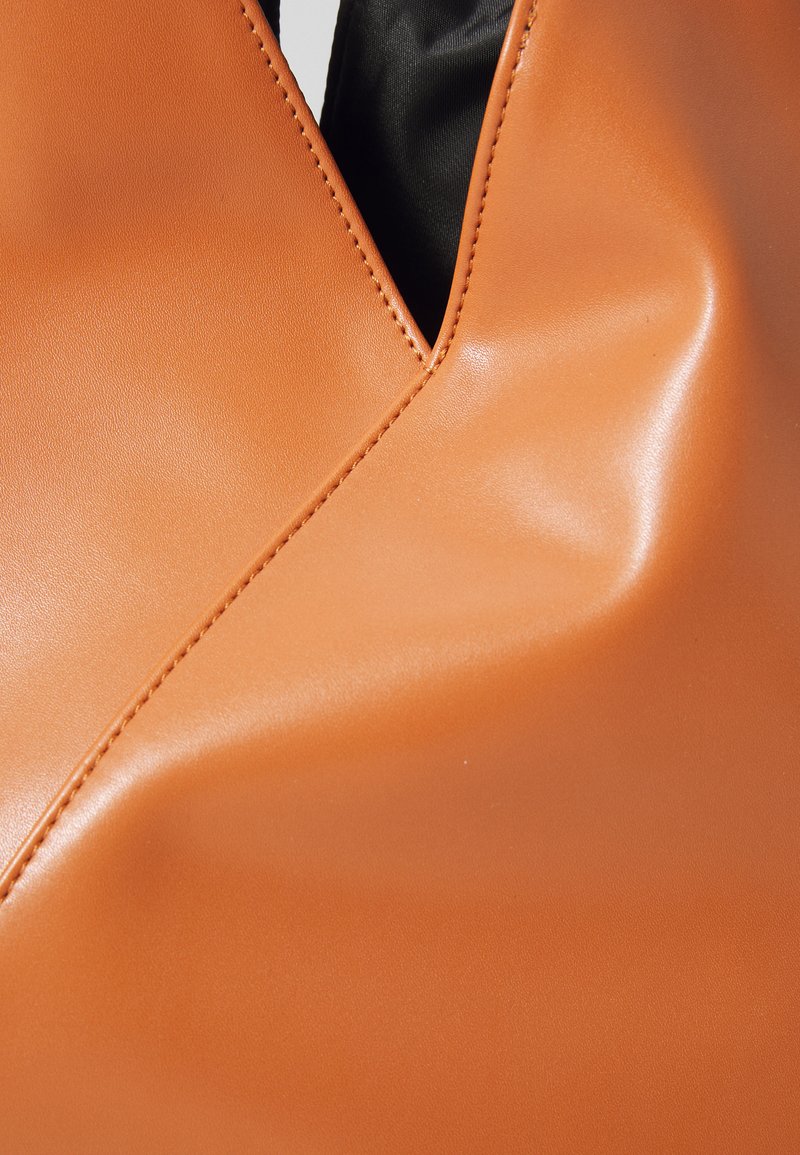 Prima di un indumento in pelle tan con cuciture visibili e un scollo a V che rivela il tessuto nero sottostante.