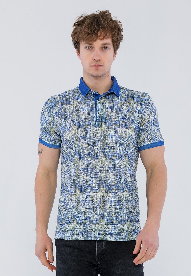 Polo de manga corta en azul con un patrón texturizado que presenta acentos en verde y blanco. Cuello y puños en azul sólido; cierre de botón.