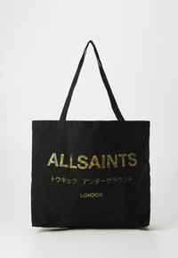 Juodas kanvos pirkinių krepšys su ilgais diržais, ant kurio užrašas "ALLSAINTS" multicolor, kamufliažinį atvaizdą primenančia šriftu ir "LONDON" aukso spalvos žemiau.
