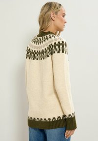 Strickpullover in Creme mit grünen und braunen gemusterten Akzenten am Halsausschnitt und Saum; gerippte Bündchen; weiche Textur; lockere Passform.
