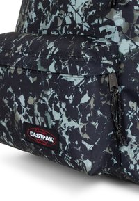 Zaino nero con motivo camouflage in tonalità di verde e blu, una tasca frontale e un'etichetta con il logo Eastpak ben visibile.