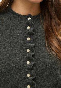 Siv pulover iz volne z okroglim izrezom, ki ima nabran sprednji del in kreme barve gumbe po sredini. Mehka tekstura in oprijet kroj.