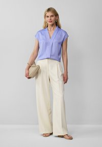 Lavendel blouse met korte mouwen en V-hals, gecombineerd met crèmekleurige broek met wijde pijpen en een beige handtas. Glad textuur en minimalistisch ontwerp.