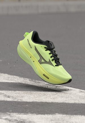 Scarpa da corsa giallo brillante con lacci e dettagli neri, a mezz'aria sopra l'asfalto, mostrando suola e dettaglio del logo laterale.