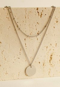 Collana d'argento con due catene di diverse lunghezze, una decorata con piccoli perline e un pendente metallico circolare con finitura spazzolata.