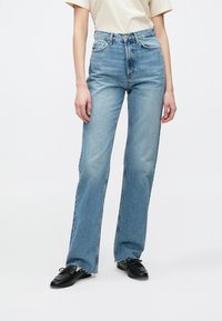 Vaqueros de denim de cintura alta en un tono azul claro, con un diseño de pierna recta, ligeras decoloraciones y dobladillo deshilachado. Presentan el estilo tradicional de cinco bolsillos.