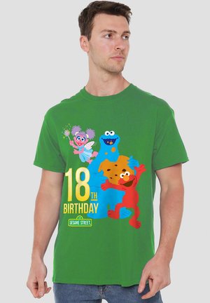 Mann trägt ein grünes T-Shirt mit den Sesamstraße-Charakteren Elmo, Krümelmonster und Abby Cadabby, die seinen 18. Geburtstag feiern.