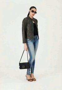 Chaqueta de cuero negra, top negro, jeans azules claros, sandalias marrones de tacón y bolso negro. Modelo con gafas de sol oscuras.