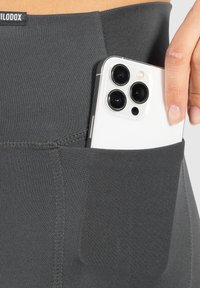 Szare legginsy wykonane z miękkiego, elastycznego materiału, z boczną kieszenią na smartfona. Widoczne są detale szwów wzdłuż brzegów.