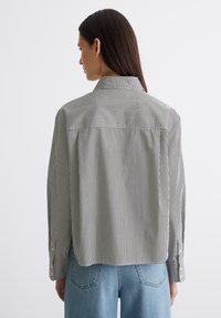 Gestreifte Hemdbluse mit Kragen, lockerer Passform, langen Ärmeln mit Knopfmanschetten und geradem Saum. Der Stoff wirkt texturiert.