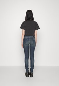 Camiseta negra de manga corta y corta, combinada con jeans ajustados de un azul oscuro. El conjunto tiene un diseño ajustado y un estilo minimalista.