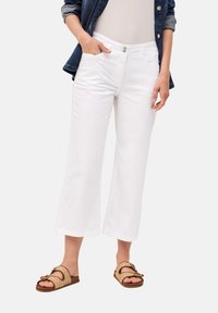 Pantalones cortos blancos de corte recto con bolsillos frontales, acompañados de sandalias texturizadas con un diseño trenzado y correas ajustables.