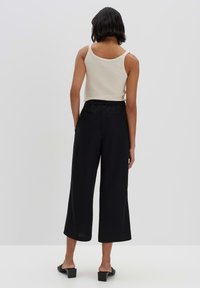 Pantalons larges noirs avec une taille élastique, associés à un débardeur en crème à côtes. Tissu lisse, design minimal et sans motifs visibles.