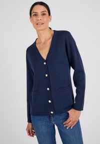 Cardigan tricoté marine avec un col en V, sept boutons dorés et deux poches frontales. Doté de poignets côtelés et d'une texture lisse.