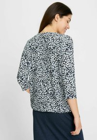 Bluse mit Blumenmuster, die einen dunkelblauen Hintergrund mit hellblauen und weißen Motiven zeigt, mit langen Ärmeln und lockerer Passform. Glatte Stoffoberfläche.