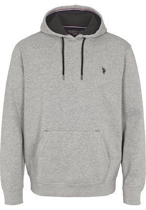 Man draagt een lichtgrijze hoodie met zwarte trekkoorden en een klein donker logo op de borst, gecombineerd met een blauwe spijkerbroek, één hand in de zak.