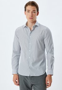 Camisa de manga larga a rayas en blanco y azul marino, hecha de tejido ligero, con un cuello abotonado y bandas de puño contrastantes.