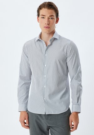 Camisa de manga larga a rayas en blanco y azul marino, hecha de tejido ligero, con un cuello abotonado y bandas de puño contrastantes.
