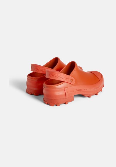 Orange gummitofflor med texturerad sula, förstärkta tår och en bakrem. Kraftiga, mönstrade sulor för bra grepp. Varumärkeslogga synlig.