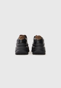 Black leather sneakers with a patterned brown leopard print on the heel. Thick, textured black rubber sole with a rounded shape.