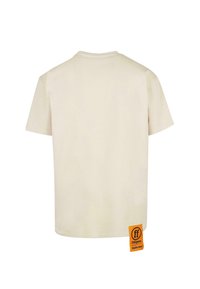 Kortermet beige t-skjorte, laget av bomull, rund hals, med et oransje merke nederst til venstre som viser merke og vektinformasjon.