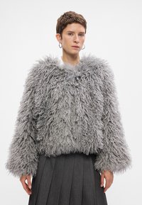 Puszysta, szara kurtka z sztucznego futra z szerokim kołnierzem i długimi, objętościowymi rękawami. Noszona na plisowanej, ciemnoszarej spódnicy.