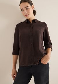 Dunkelbraunes Button-up-Hemd mit Kragen, hochgekrempelten Ärmeln und subtiler Glanz. Verfügt über Vorderknöpfe und Stickdetails.