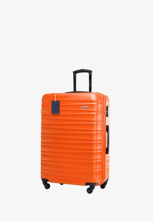 Orange Hartschalenkoffer mit vertikalen Rillen, ausziehbarem schwarzen Griff, vier Rädern und einem befestigten blauen Gepäcketikett.