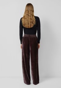 Donkerpaarse fluwelen wijde broek met een elastische tailleband, van achteren getoond. Glad oppervlak met een comfortabele pasvorm.