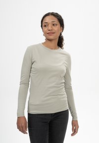 Helles graues Langarm-T-Shirt aus weichem Stoff, runder Ausschnitt, körperbetonter Schnitt, kombiniert mit dunklen Jeans, präsentiert auf einem neutralen Hintergrund.