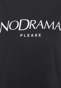 Czarna bawełniana koszulka z odważnym białym napisem "NO DRAMA PLEASE" w mieszance wielkich i małych liter.