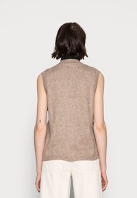 Pull sans manches marron avec une texture côtelée, col rond et coupe décontractée, assorti à un pantalon de couleur claire.
