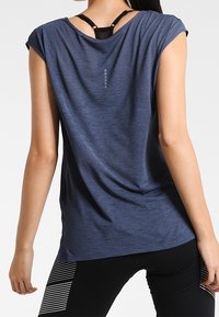 Modré sportovní tričko s krátkými rukávy, texturovaná látka a design na zadní straně s výřezem ve tvaru klíčové dírky a zvýrazněným švem.