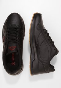 Schwarze Sportschuhe mit einem glatten Lederobermaterial, Gummisohle und rotem Branding; verfügen über ein Schnürdesign und subtile seitliche Konturen.