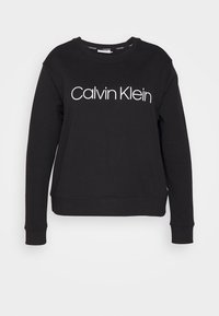Černá mikina s dlouhými rukávy a kulatým výstřihem, která má na přední straně bílé logo "Calvin Klein" v moderním písmu. Měkká textura.