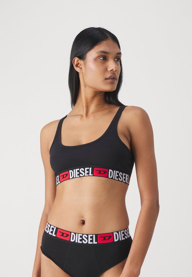 Černý bavlněný bralet s širokým červeným a bílým elastickým páskem s logem dole. Odpovídající vysoké kalhotky, hladká textura a minimalistický design.