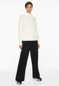 White ribbed sweater with a high collar and half-zip, paired with black wide-leg trousers and black sneakers.