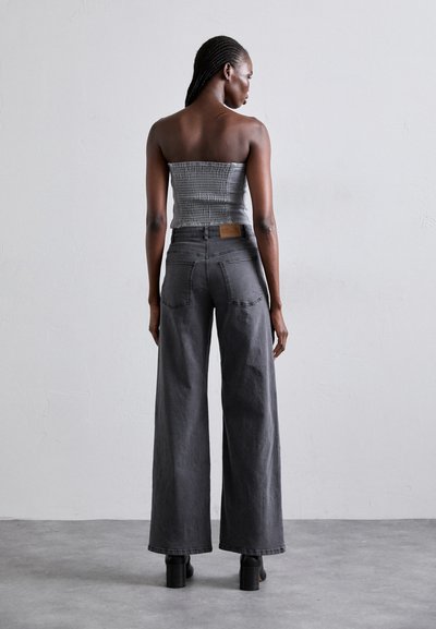 Gray strapless top with textured fabric paired with wide-leg gray pants. Notable features include a leather tag at the back and heeled boots.