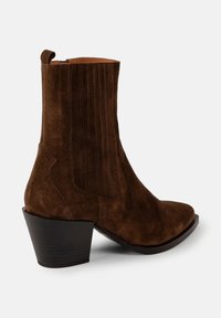 Botină din suede maro, cu toc gros stivuit, vârf rotunjit, cusătură verticală pe tijă și buclă de prindere în spate.