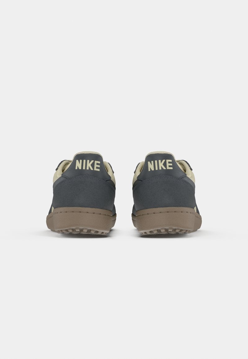 Nike sneakers hebben een grijs suède bovenwerk met een crème-kleurige hiel, twee opvallende "Nike" logo's en een gestructureerde bruine rubberen zool.