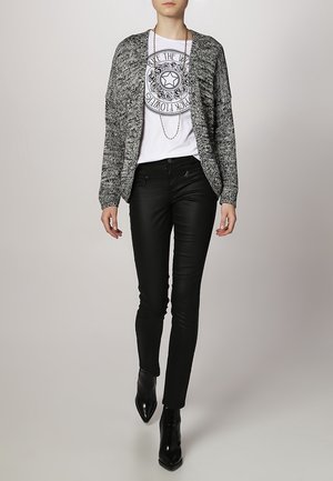 Czarnobiały dziergany sweter na guziki nałożony na graficzny t-shirt, zestawiony z dopasowanymi czarnymi dżinsami i czarnymi botkami na szpic. Prosty srebrny naszyjnik.