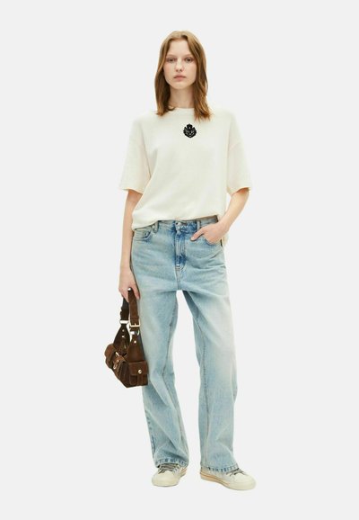 Witte, gestructureerde oversized t-shirt met zwarte bloemenpatch, lichtblauwe losse denim jeans en een bruine suède schoudertas. Inclusief casual schoeisel.
